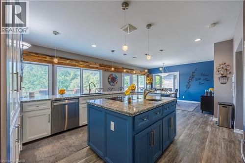 Two tone kitchen featuring light stone counters, stainless steel dishwasher, dark wood-style floors, pendant lighting, and an island with sink - 1285 Cockshutt Road, Simcoe, ON - Indoor Photo Showing Kitchen With Stainless Steel Kitchen