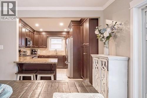 Kitchen with stainless steel appliances, a peninsula, light stone countertops, a breakfast bar area, and light tile patterned floors - 143 Huxley Avenue S, Hamilton, ON - Indoor