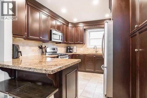 Kitchen with dark wood finish cabinetry, a peninsula, stainless steel appliances, decorative backsplash, and light stone countertops - 143 Huxley Avenue S, Hamilton, ON - Indoor Photo Showing Kitchen