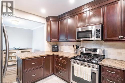 Kitchen featuring stainless steel appliances, light stone countertops, crown molding, backsplash, and a peninsula - 143 Huxley Avenue S, Hamilton, ON - Indoor Photo Showing Kitchen