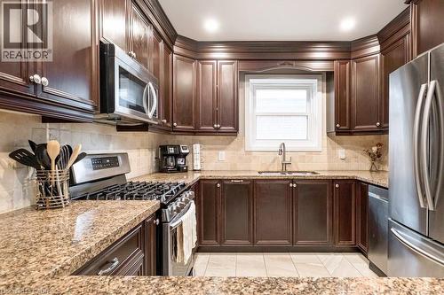 Kitchen featuring stainless steel appliances, light stone counters, dark wood finish cabinetry, and decorative backsplash - 143 Huxley Avenue S, Hamilton, ON - Indoor Photo Showing Kitchen With Double Sink