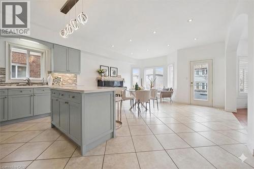 Open-concept kitchen and dining area featuring light-toned cabinetry, a central island with countertop seating, tiled flooring, and multiple windows - 512 Wood Nettle Way, Waterloo, ON - Indoor Photo Showing Kitchen