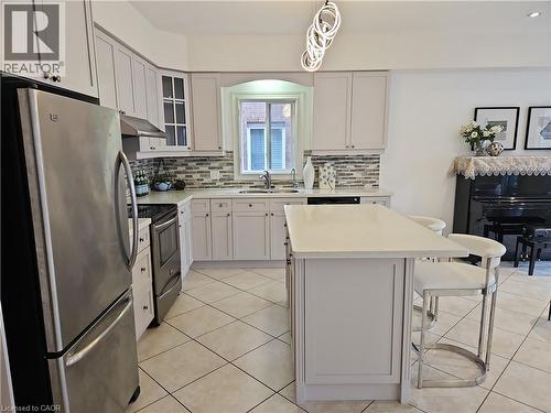 Kitchen featuring stainless steel appliances, light cabinetry, a mosaic tile backsplash, a center island with countertop seating, and light-toned tile flooring - 512 Wood Nettle Way, Waterloo, ON - Indoor Photo Showing Kitchen