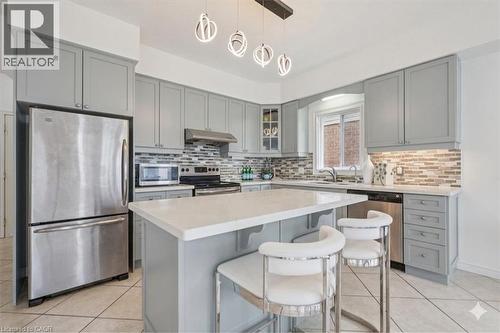 Contemporary kitchen featuring a central island with a light-toned countertop, light grey cabinetry, tile flooring, stainless steel appliances, and a mosaic tile backsplash - 512 Wood Nettle Way, Waterloo, ON - Indoor Photo Showing Kitchen With Upgraded Kitchen
