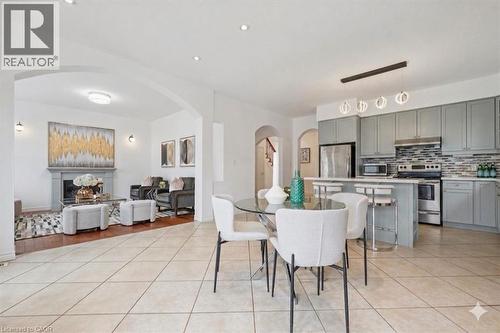 Open-concept living space with light-toned tile flooring, a kitchen featuring grey cabinetry and stainless steel appliances, a breakfast bar with seating, a dedicated dining area, and an arched entryw - 512 Wood Nettle Way, Waterloo, ON - Indoor