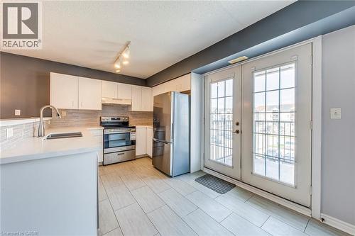 Kitchen with stainless steel appliances, backsplash, white cabinetry, light stone countertops, and french doors - 1411 Walker'S Line Unit# 302, Burlington, ON - Indoor Photo Showing Kitchen With Double Sink