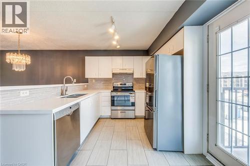 Kitchen with decorative backsplash, stainless steel appliances, a peninsula, white cabinets, and a chandelier - 1411 Walker'S Line Unit# 302, Burlington, ON - Indoor Photo Showing Kitchen With Double Sink