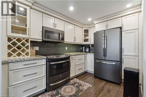 Kitchen with glass fronted cabinets, stainless steel appliances, white cabinetry, dark wood-type flooring, and light stone countertops - 27 Red Clover Crescent, Kitchener, ON - Indoor Photo Showing Kitchen With Stainless Steel Kitchen