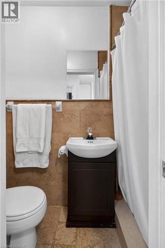 Full bathroom featuring a shower with curtain, vanity, tile walls, stone tile flooring, and wainscoting - 216 Robert Street, Hamilton, ON - Indoor Photo Showing Bathroom