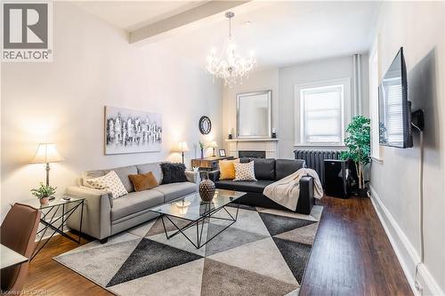 Living area with wood finished floors, a chandelier, beamed ceiling, and radiator heating unit - 14 Duke Street, Hamilton, ON - Indoor Photo Showing Living Room