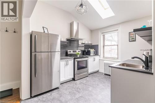 Kitchen with stainless steel appliances, white cabinets, range hood, vaulted ceiling, and a skylight - 14 Duke Street, Hamilton, ON - Indoor Photo Showing Kitchen