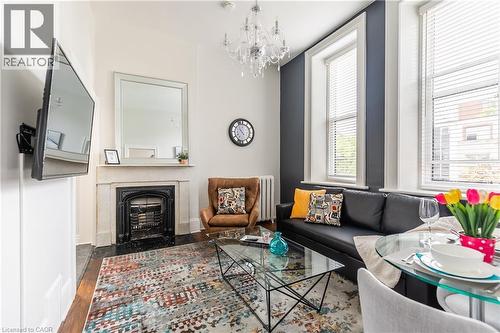 Living room featuring a fireplace with flush hearth, a chandelier, radiator heating unit, and wood finished floors - 14 Duke Street, Hamilton, ON - Indoor With Fireplace