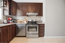 Kitchen featuring stainless steel appliances, dark wood finish cabinets, light stone countertops, and decorative backsplash - 