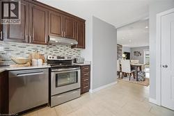 Kitchen featuring dark wood finish cabinets, stainless steel appliances, light stone counters, and backsplash - 