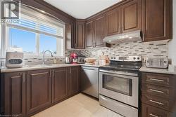 Kitchen with stainless steel appliances, dark wood finish cabinets, decorative backsplash, and light stone countertops - 