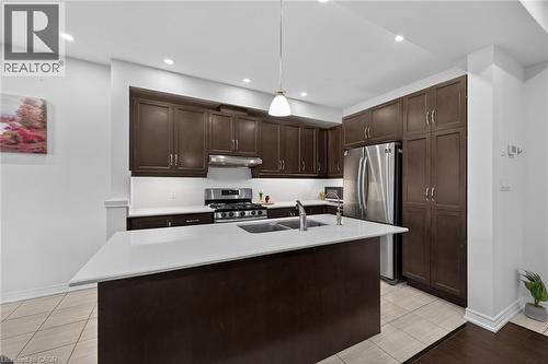 Kitchen with dark wood finish cabinetry, stainless steel appliances, a kitchen island with sink, light stone countertops, and hanging light fixtures - 80 Severino Circle, Smithville, ON - Indoor Photo Showing Kitchen With Double Sink