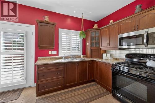 Kitchen with black range with gas stovetop, stainless steel microwave, glass fronted cabinets, tasteful backsplash, and light tile patterned floors - 48 Hallmark Trail, Hamilton, ON - Indoor Photo Showing Kitchen With Double Sink