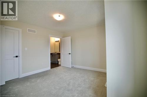 Unfurnished bedroom featuring a textured ceiling, light carpet, and connected bathroom - 559 Balsam Poplar Street, Waterloo, ON - Indoor Photo Showing Other Room