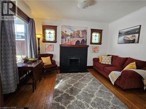 Living area featuring a brick fireplace, dark wood-type flooring, ornamental molding, and plenty of natural light - 253 Grosvenor Avenue S, Hamilton, ON - Indoor Photo Showing Living Room With Fireplace