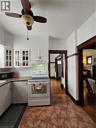 Kitchen with white electric range, backsplash, white cabinetry, a ceiling fan, and black microwave - 253 Grosvenor Avenue S, Hamilton, ON - Indoor Photo Showing Kitchen