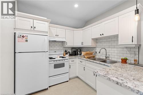 Kitchen featuring white appliances, decorative backsplash, white cabinets, and light stone countertops - 58 Hohner Avenue, Kitchener, ON - Indoor Photo Showing Kitchen With Double Sink