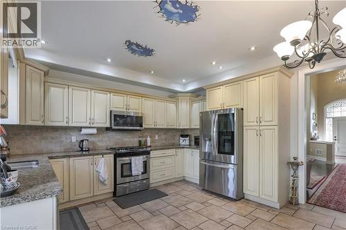 Kitchen featuring stainless steel appliances, dark stone countertops, cream cabinetry, hanging lights, and decorative backsplash - 254 Rymal Road W, Hamilton, ON - Indoor Photo Showing Kitchen With Double Sink
