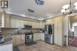 Kitchen featuring stainless steel appliances, dark stone countertops, cream cabinetry, hanging lights, and decorative backsplash - 