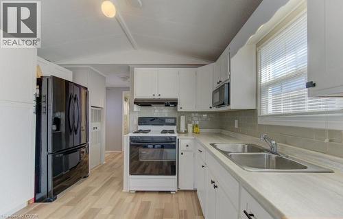 Kitchen featuring light countertops, black appliances, white cabinets, light wood finished floors, and decorative backsplash - 580 Beaver Creek Road Unit# 185, Waterloo, ON - Indoor Photo Showing Kitchen With Double Sink
