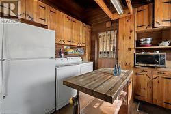 Kitchen featuring freestanding refrigerator, wood walls, open shelves, stainless steel microwave, and brown cabinetry - 