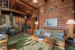 Carpeted living area with wood walls, a wood stove, wooden ceiling, and ceiling fan - 
