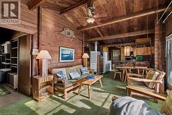 Living room with wood walls, carpet flooring, a ceiling fan, wood ceiling, and a wood stove - 