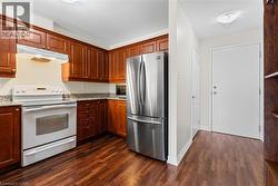 Kitchen featuring white electric range oven, freestanding refrigerator, dark wood-style flooring, and light stone counters - 