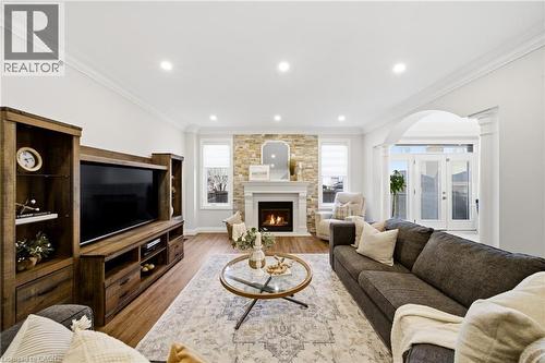 Living area featuring arched walkways, ornamental molding, french doors, light wood finished floors, and a lit fireplace - 4670 Bracknell Road, Burlington, ON - Indoor Photo Showing Living Room With Fireplace