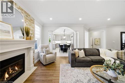 Living area featuring ornamental molding, arched walkways, a glass covered fireplace, decorative columns, and wood finished floors - 4670 Bracknell Road, Burlington, ON - Indoor Photo Showing Living Room With Fireplace