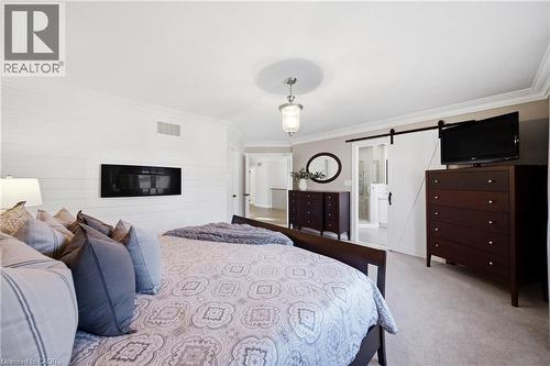 Bedroom featuring light carpet, ornamental molding, a barn door, and ensuite bathroom - 4670 Bracknell Road, Burlington, ON - Indoor Photo Showing Bedroom