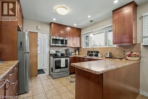 Kitchen with a peninsula, stainless steel appliances, decorative backsplash, light tile patterned flooring, and pendant lighting - 11 Carwyn Crescent, Hamilton, ON - Indoor Photo Showing Kitchen