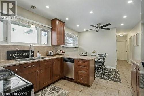 Kitchen featuring a peninsula, black range with electric stovetop, decorative backsplash, stainless steel dishwasher, and light tile patterned floors - 11 Carwyn Crescent, Hamilton, ON - Indoor Photo Showing Kitchen With Double Sink