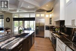 Kitchen with stainless steel appliances, coffered ceiling, glass fronted cabinets, two tone color scheme, and light wood-style floors - 