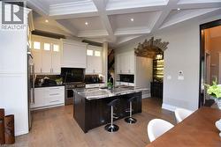 Kitchen with a kitchen bar, coffered ceiling, a center island with sink, premium appliances, and backsplash - 