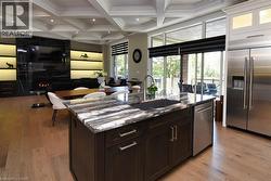 Kitchen with coffered ceiling, stainless steel appliances, open floor plan, dark wood finish cabinetry, and light wood-style floors - 