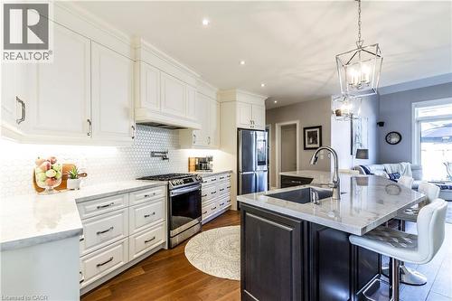 Two tone kitchen featuring a center island with sink, light stone counters, stainless steel appliances, a kitchen breakfast bar, and dark wood finished floors - 72 Pond View Gate, Waterdown, ON - Indoor Photo Showing Kitchen With Upgraded Kitchen
