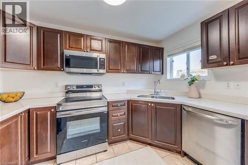 Kitchen featuring stainless steel appliances, dark wood finish cabinetry, and light tile patterned floors - 5811 Page Crescent, Burlington, ON - Indoor Photo Showing Kitchen With Double Sink