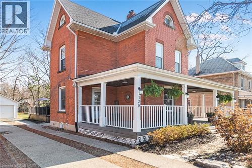 View of front facade featuring brick siding, covered porch, a detached garage, a chimney, and roof with shingles - 120 Caithness Street E, Caledonia, ON - Outdoor With Deck Patio Veranda