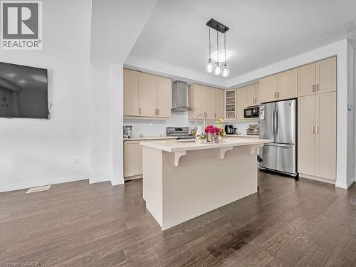 Kitchen featuring stainless steel appliances, cream cabinetry, a center island with sink, a breakfast bar area, and glass fronted cabinets - 30 Times Square Boulevard, Hamilton, ON - Indoor Photo Showing Kitchen