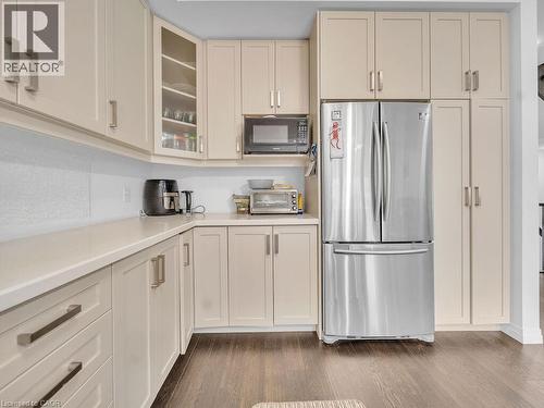 Kitchen featuring glass fronted cabinets, freestanding refrigerator, black microwave, dark wood finished floors, and cream cabinetry - 30 Times Square Boulevard, Hamilton, ON - Indoor Photo Showing Kitchen