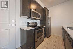 Kitchen featuring stainless steel appliances, dark wood finish cabinets, light countertops, and light tile patterned floors - 