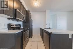 Kitchen with stainless steel appliances, a peninsula, light countertops, dark wood finish cabinetry, and a textured ceiling - 