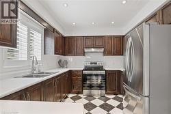 Kitchen featuring stainless steel appliances, light countertops, backsplash, recessed lighting, and dark wood finish cabinets - 