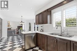 Kitchen with dark wood finish cabinets, stainless steel dishwasher, light countertops, and backsplash - 