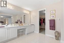 Ensuite bathroom featuring double vanity, a walk in closet, and light tile patterned floors - 